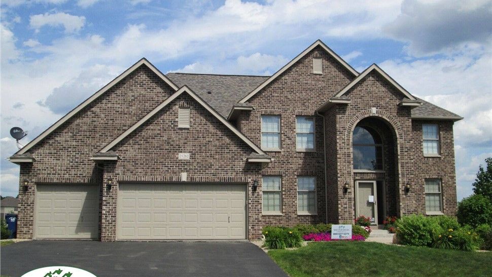Brick house with two-car garage, arched entry, and green lawn under a partly cloudy sky.