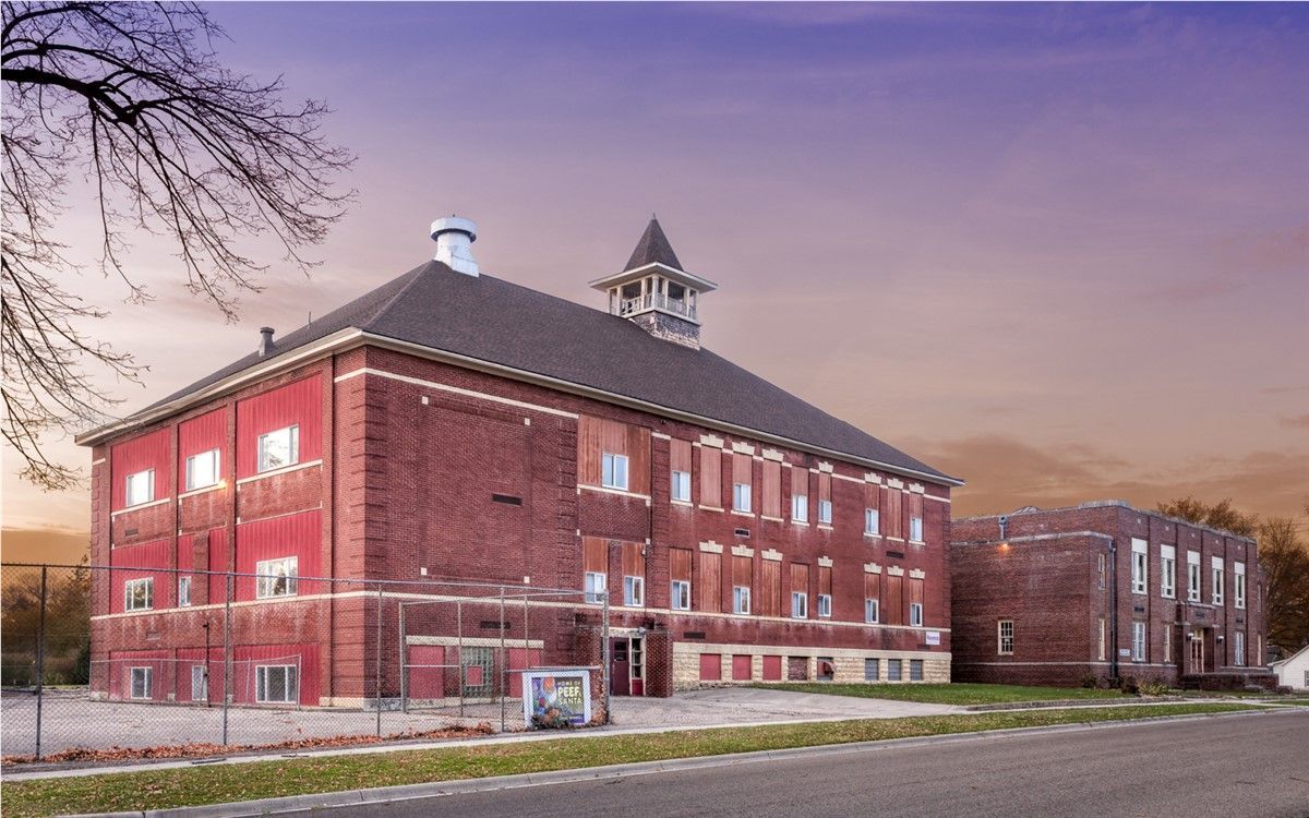 Red brick school building with a bell tower, in front of a colorful sky.