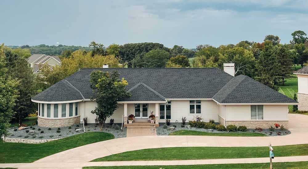 White house with dark roof and circular window section; lush lawn, driveway.