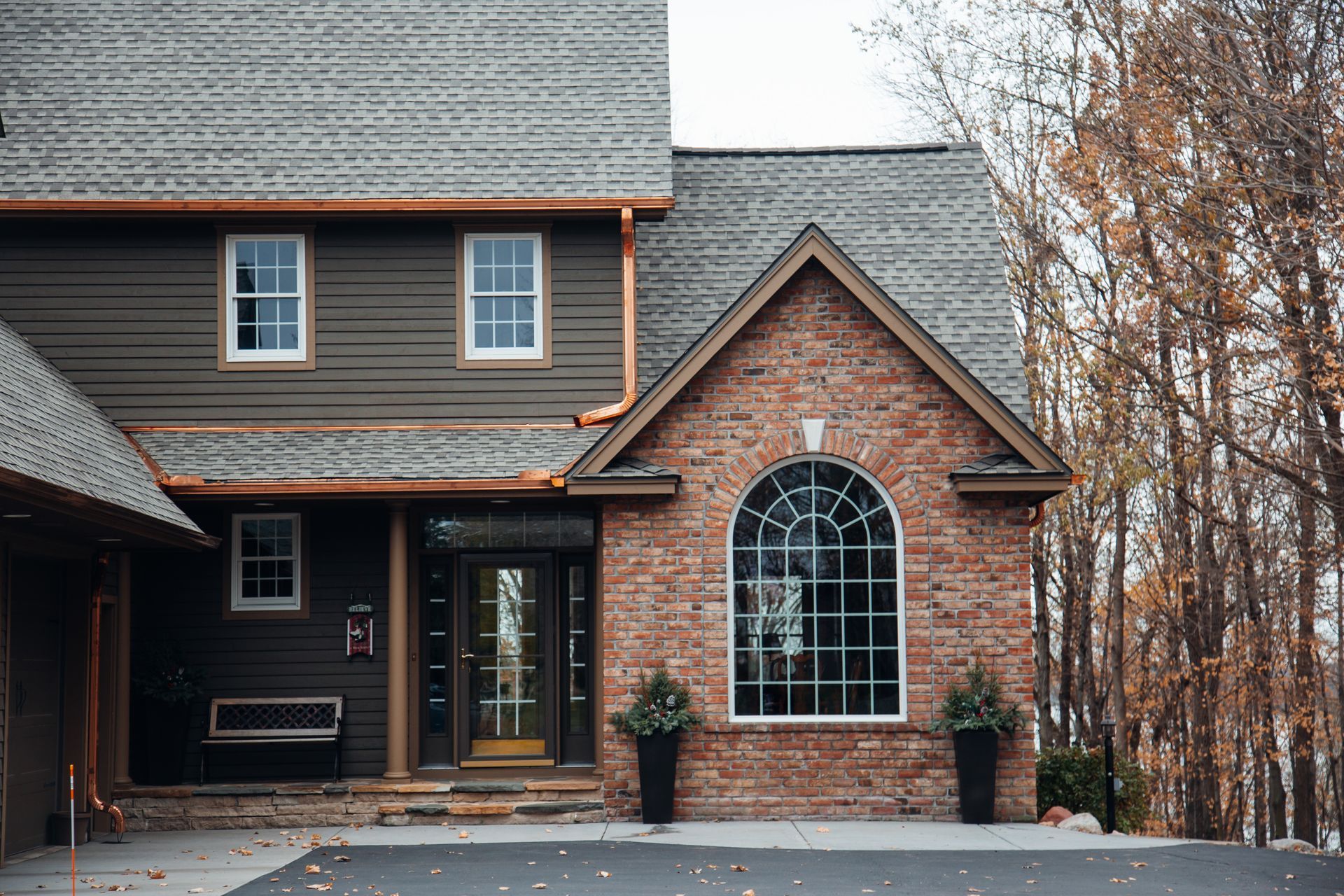 Brown brick and siding house with arched window and front door, autumn trees.