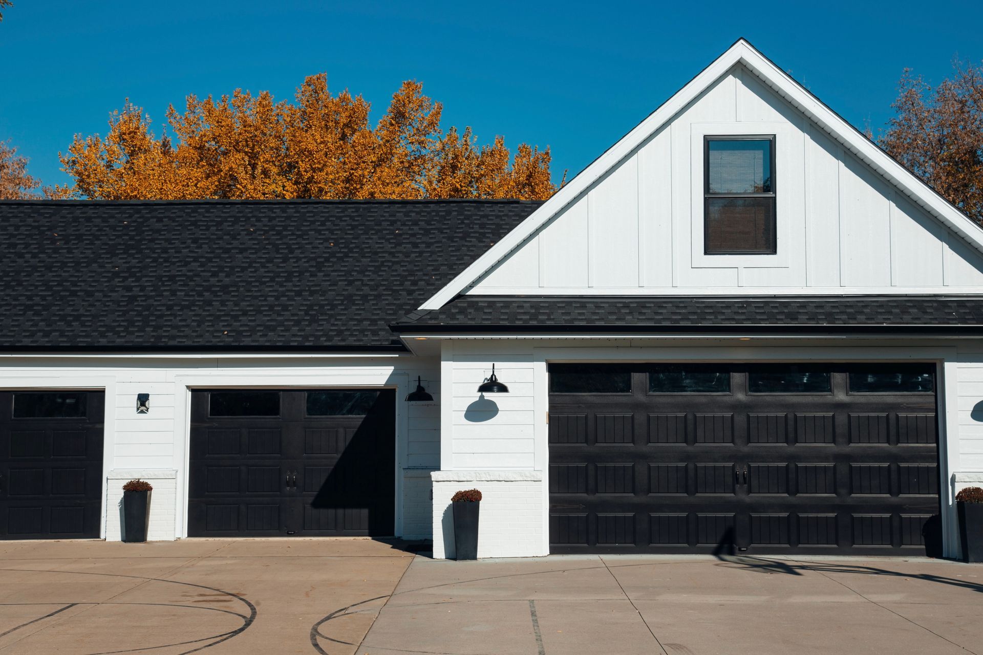 White house with black garage doors, blue sky, fall foliage.