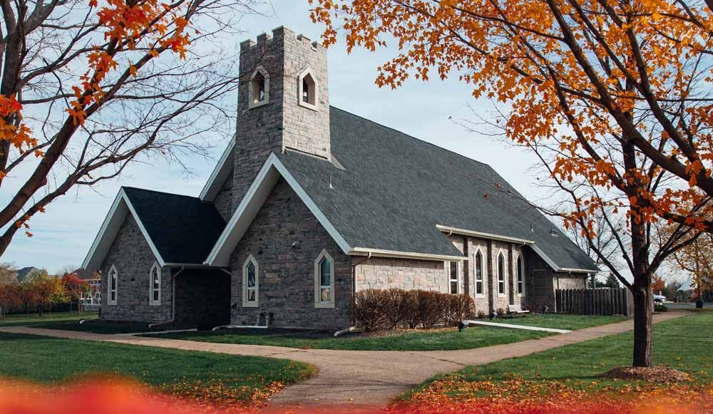Stone church building with tower, surrounded by trees with fall foliage.