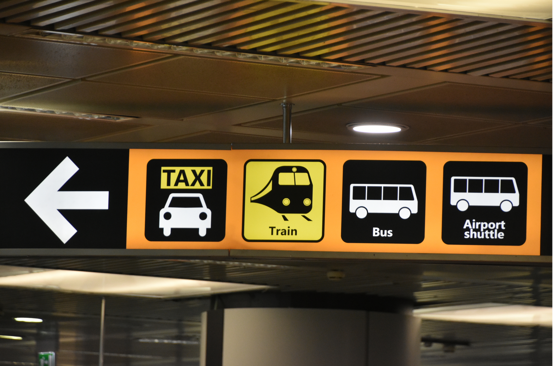 Sign indicating directions for taxi, train, bus, and airport shuttle, with a left-pointing arrow.