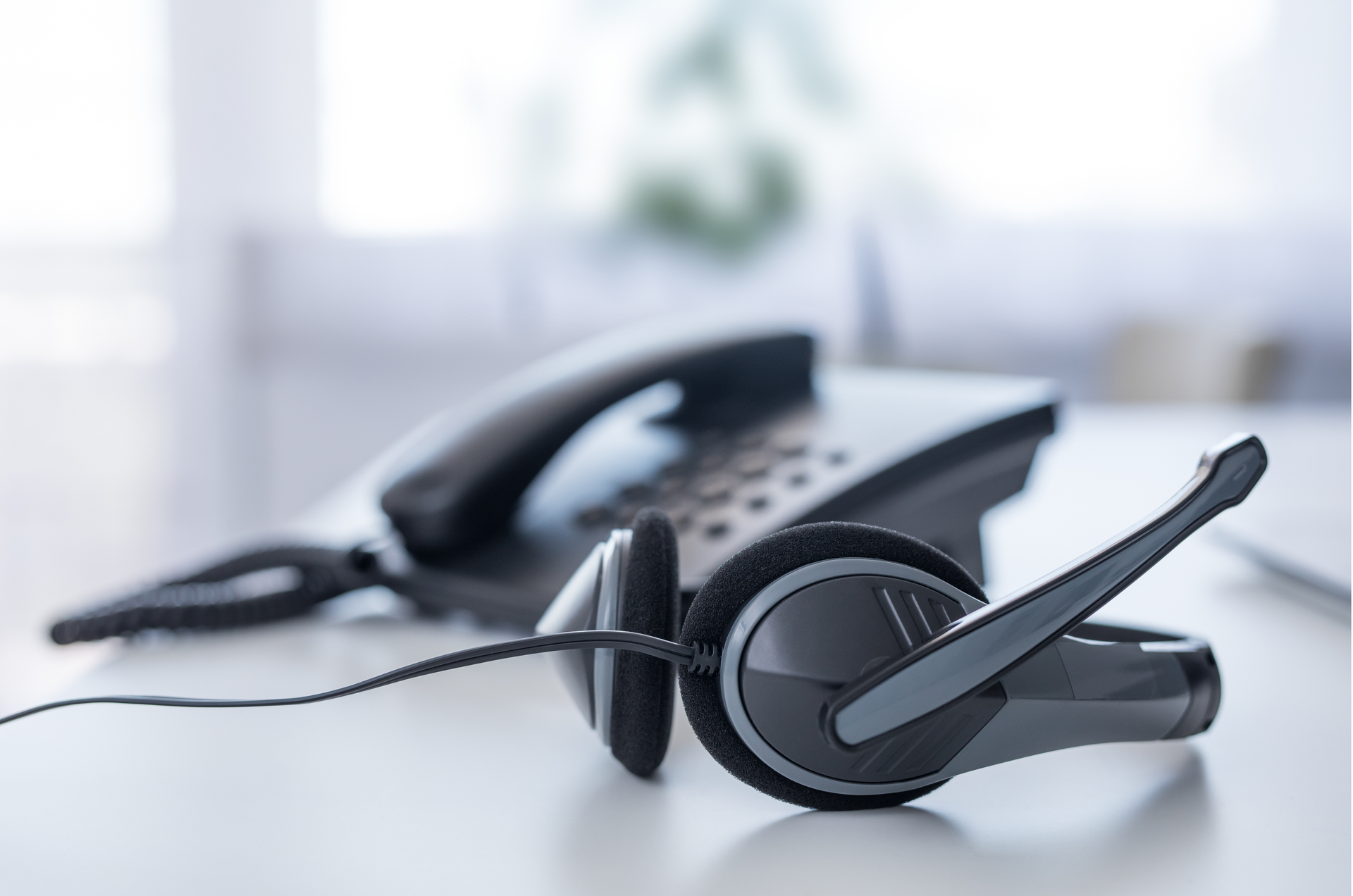 Black telephone and headset on a white desk, in an office setting.