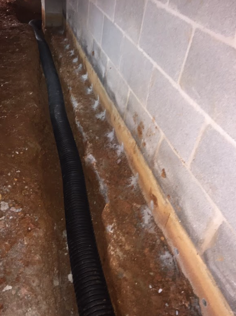 A drain pipe is being installed in a basement next to a brick wall.