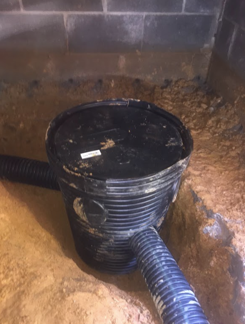 A black bucket is sitting on top of a pile of dirt next to a hose.