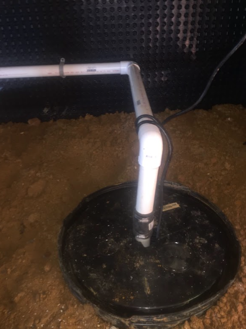 A white pipe is connected to a black bucket in a basement.