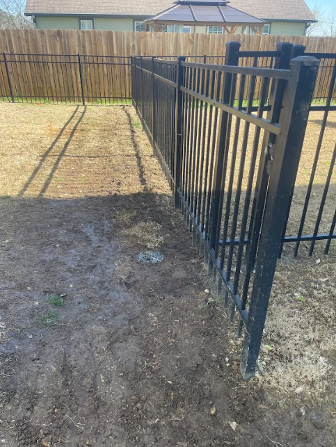 A black metal fence with a wooden fence in the background.
