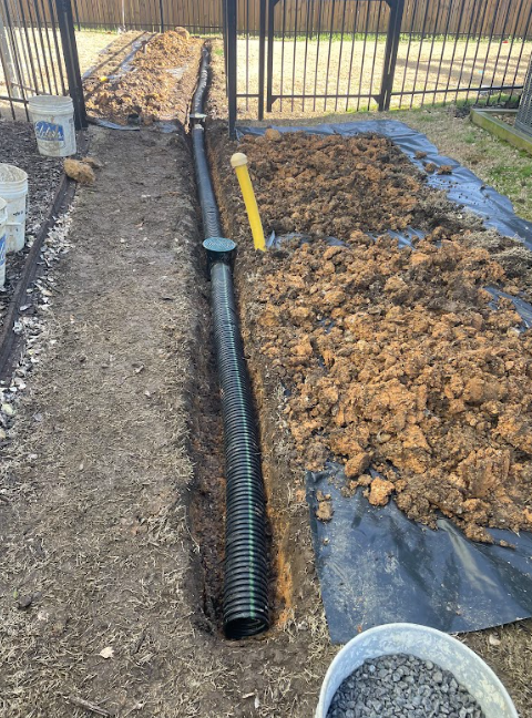 A drain pipe is being installed in the dirt in a backyard.