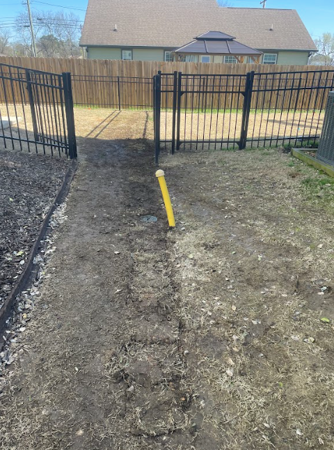 A yellow pole is in the middle of a dirt field next to a fence.