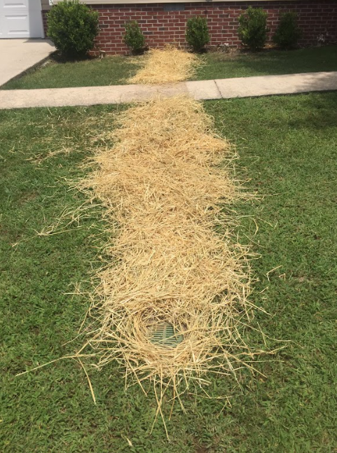 A pile of hay is laying on the grass in front of a house.