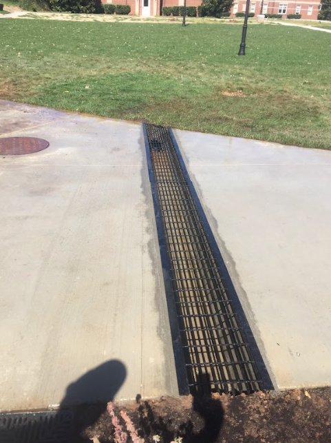 A person is standing on a sidewalk next to a drain.