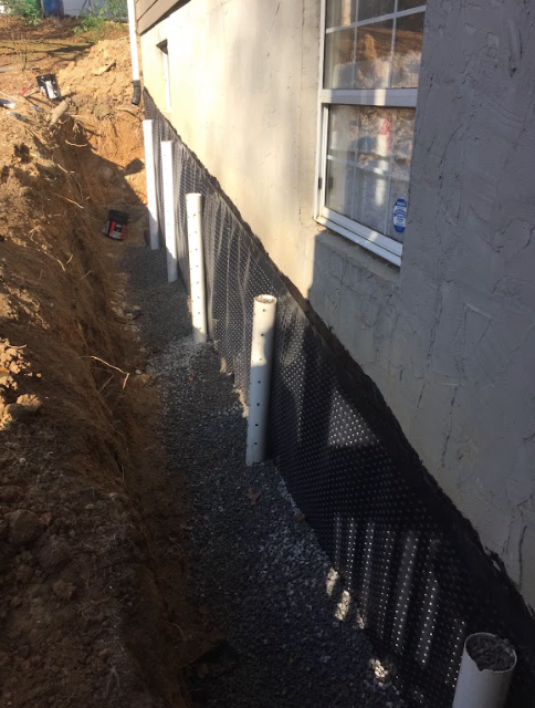 A drainage system is being installed on the side of a house