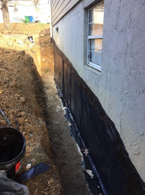 A person is painting the side of a house with black paint.