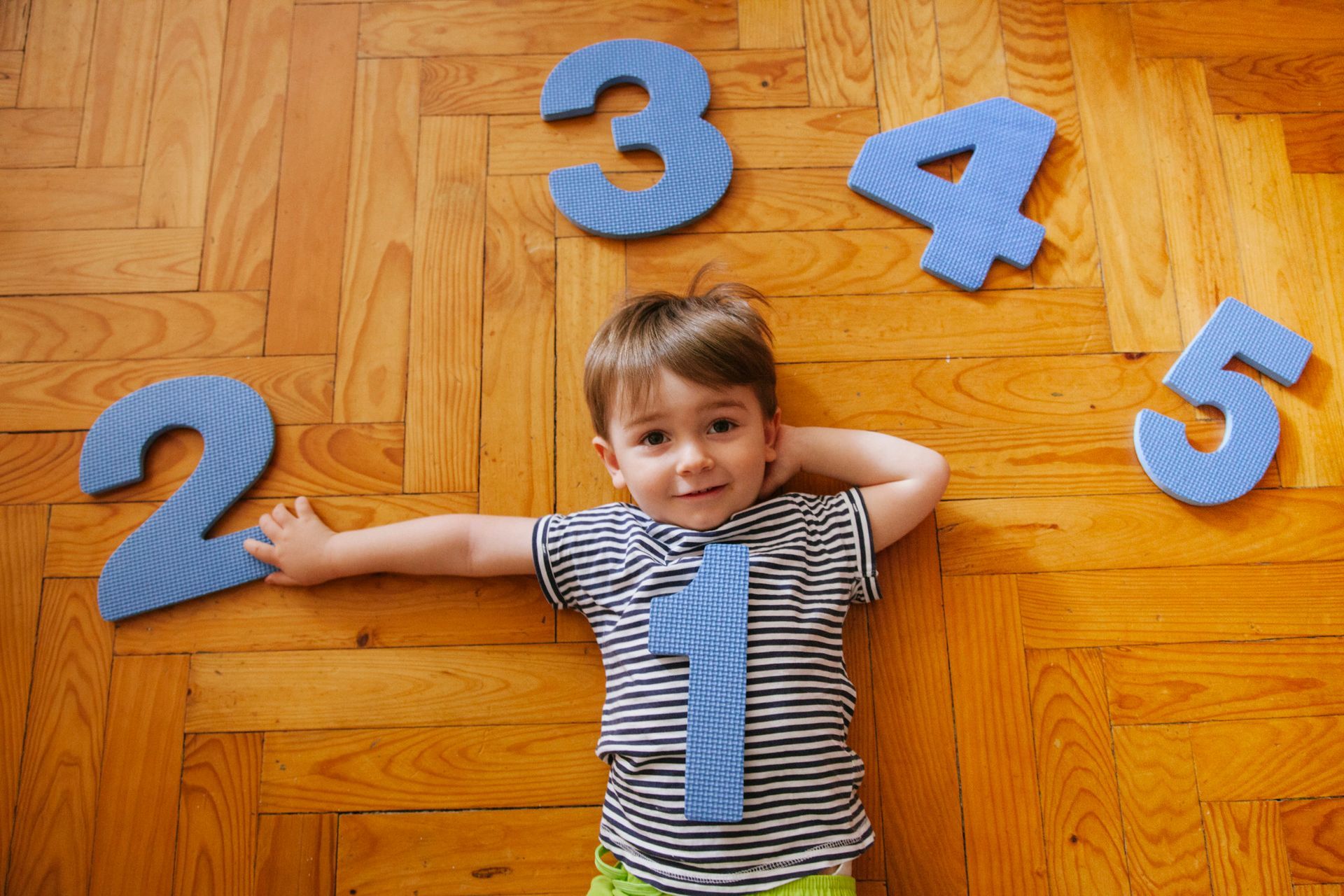 A young boy is laying on the floor surrounded by numbers.