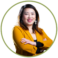 A photo of a smiling young asian woman in a mustard blazer with her arms crossed