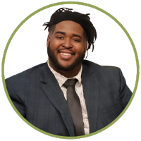 A photo of a smiling black man in a grey suit and tie.