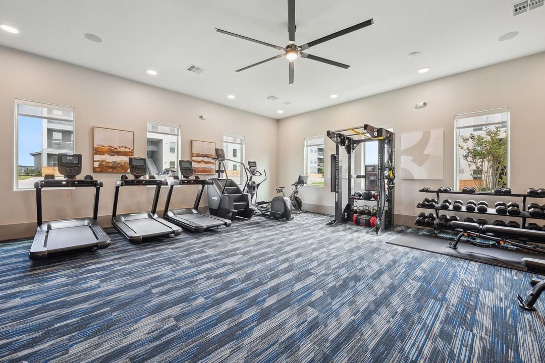 A large gym with treadmills , exercise bikes , and a ceiling fan.