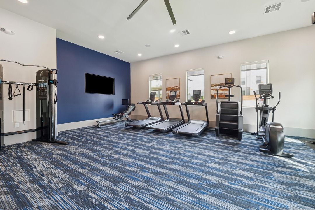 A gym with treadmills , ellipticals , and a television.