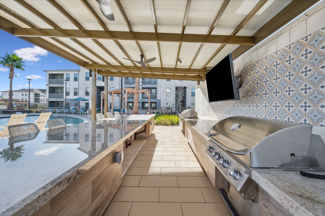 A large outdoor kitchen with a grill and a pool in the background.