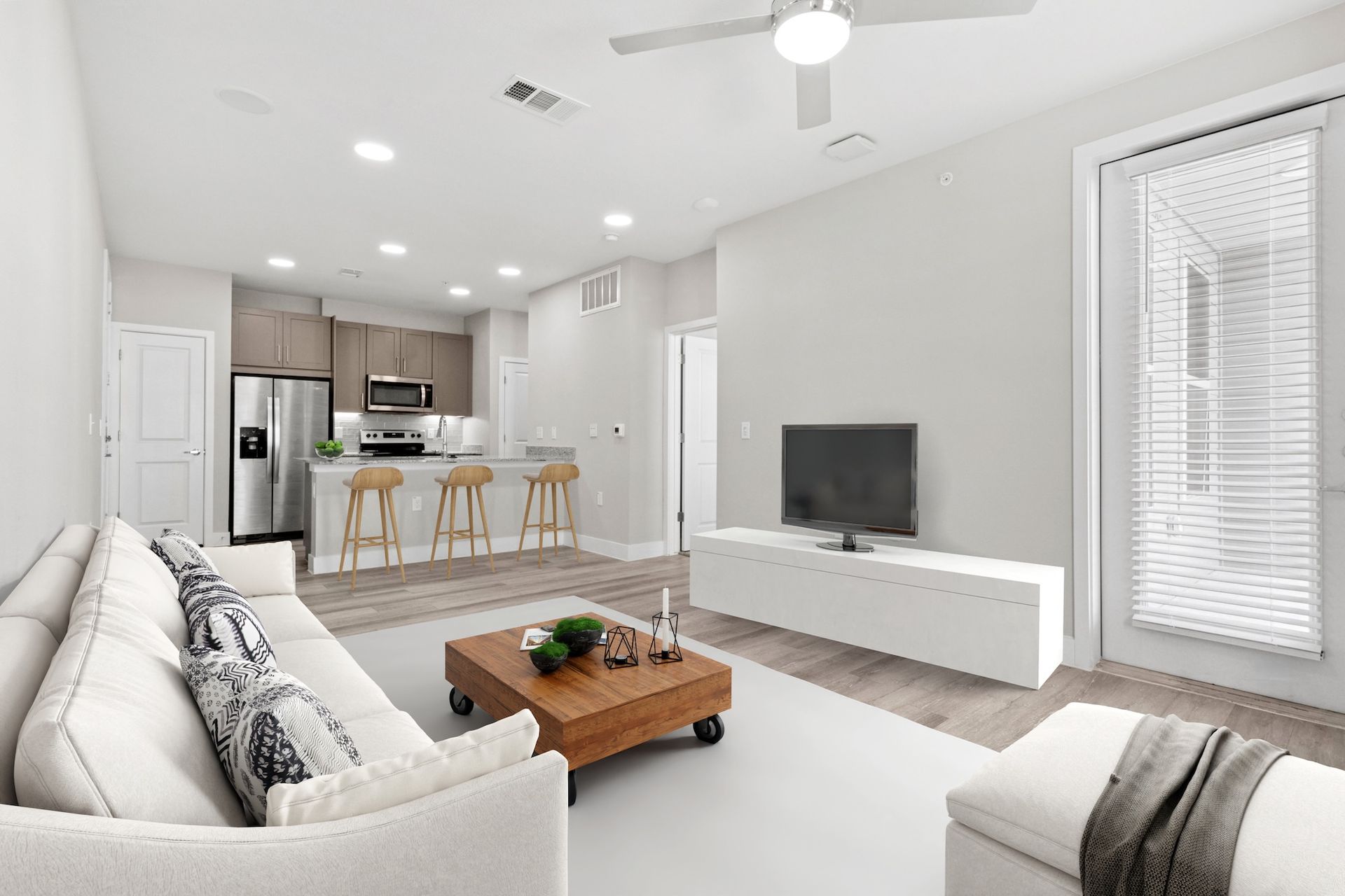 Bright living room with kitchen in the background. White couch, TV, and coffee table.