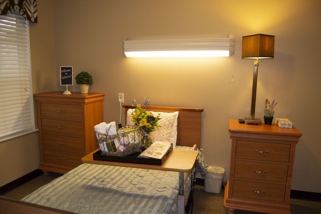 A hospital room with a bed , nightstand , dresser and lamp.
