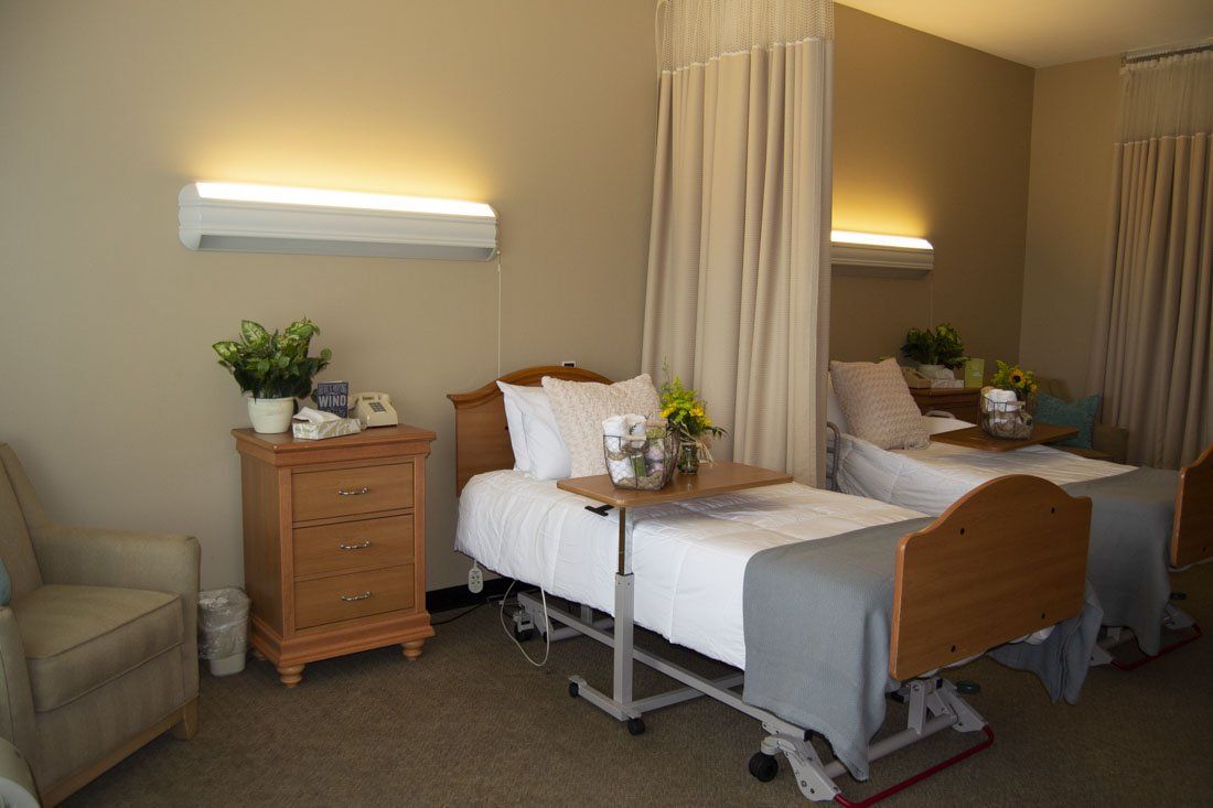 A hospital room with two beds , a nightstand , and a chair.
