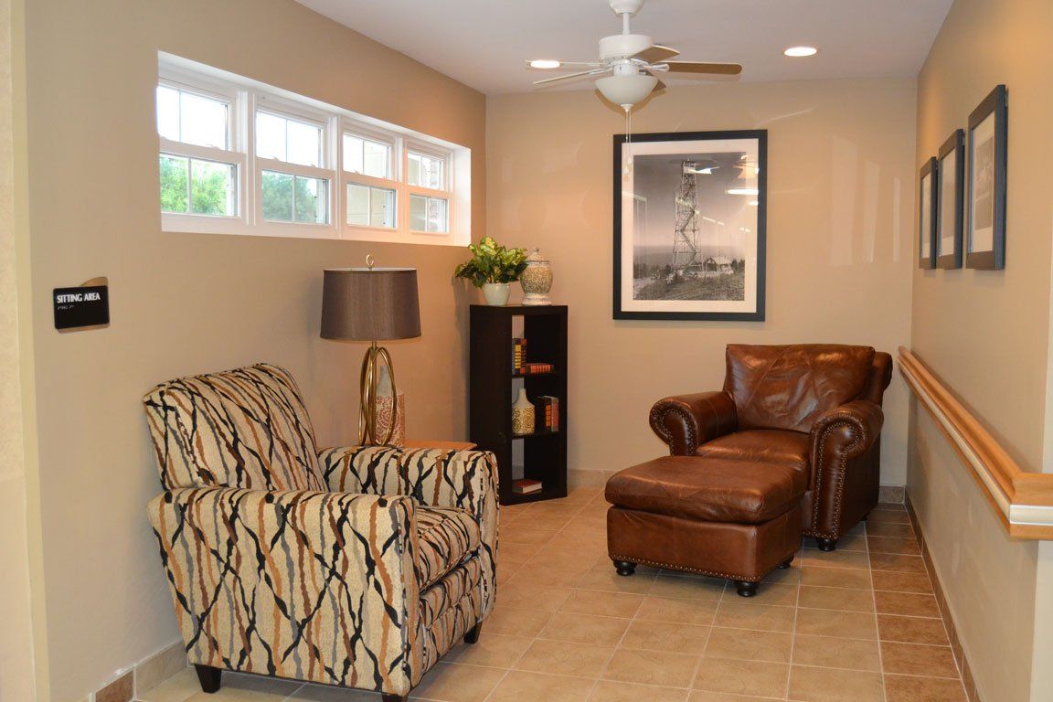A living room with two chairs and an ottoman and a ceiling fan.