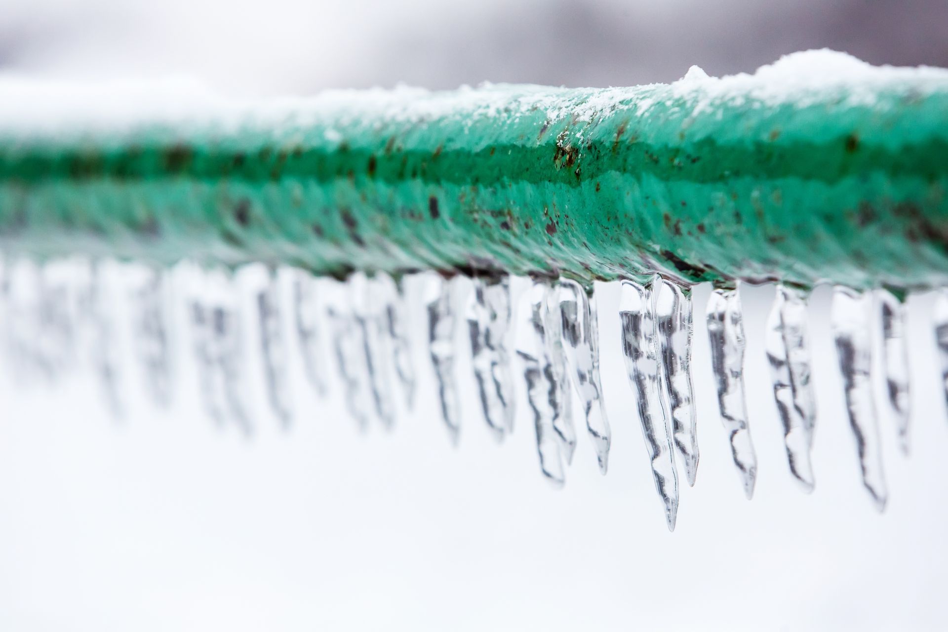 A frozen green down pipe with icicles.