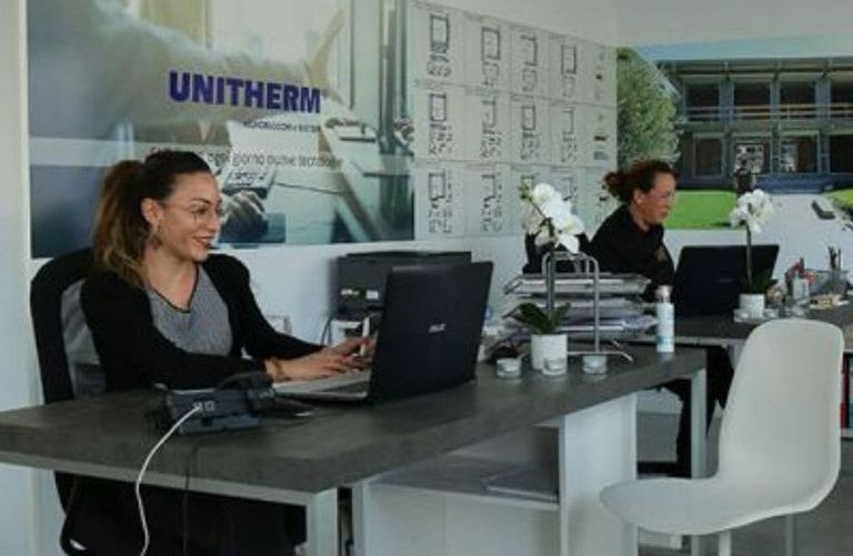 Una donna è seduta a una scrivania con un computer portatile davanti a un cartello che dice unitherm