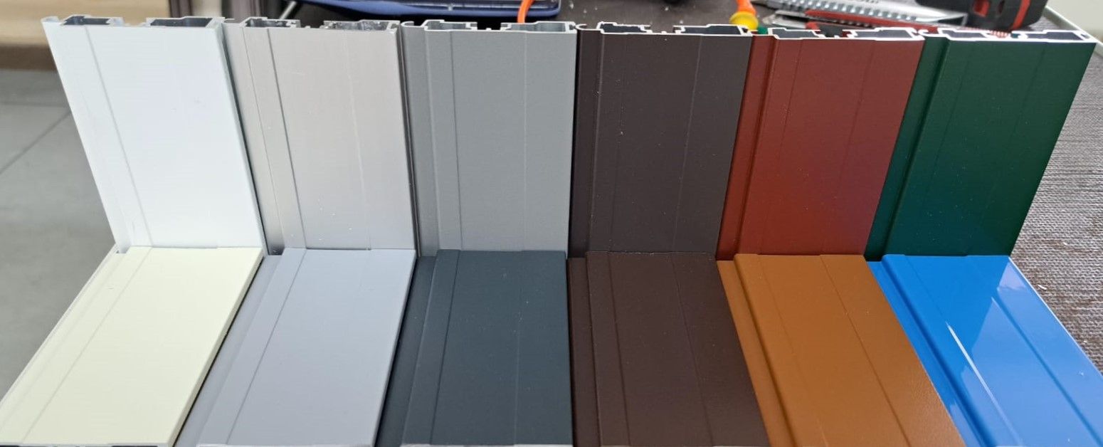 Una fila di profili in alluminio di diversi colori sono allineati su un tavolo.