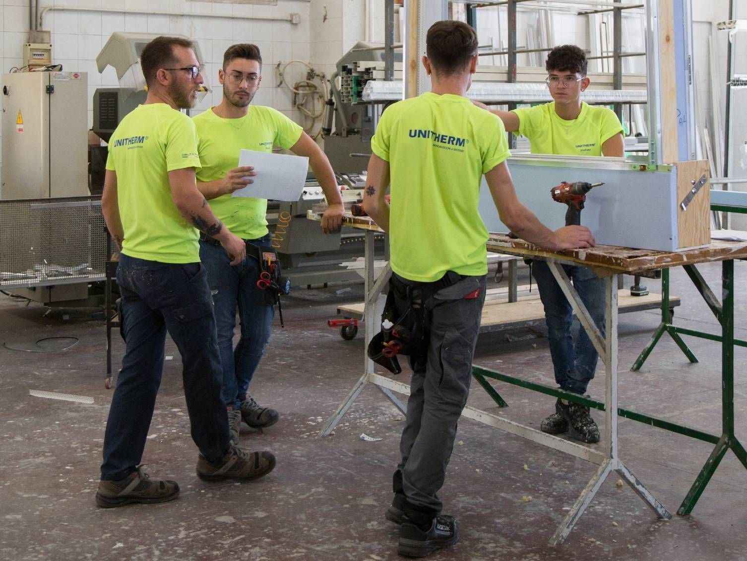 Un gruppo di uomini che indossano camicie giallo neon si trova in una fabbrica.