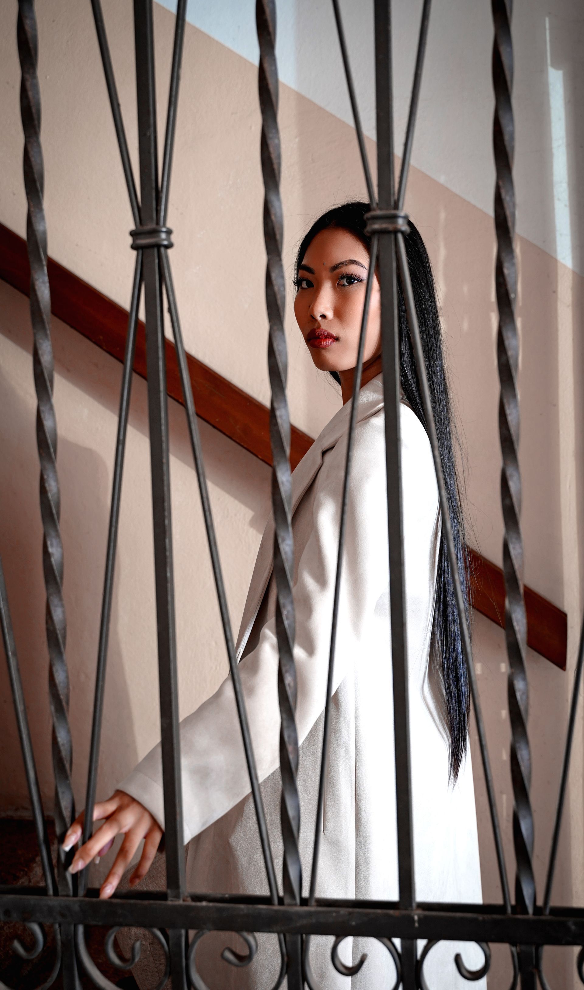 Donna in camice bianco, con lunghe trecce, dietro una ringhiera in ferro battuto su una scala.