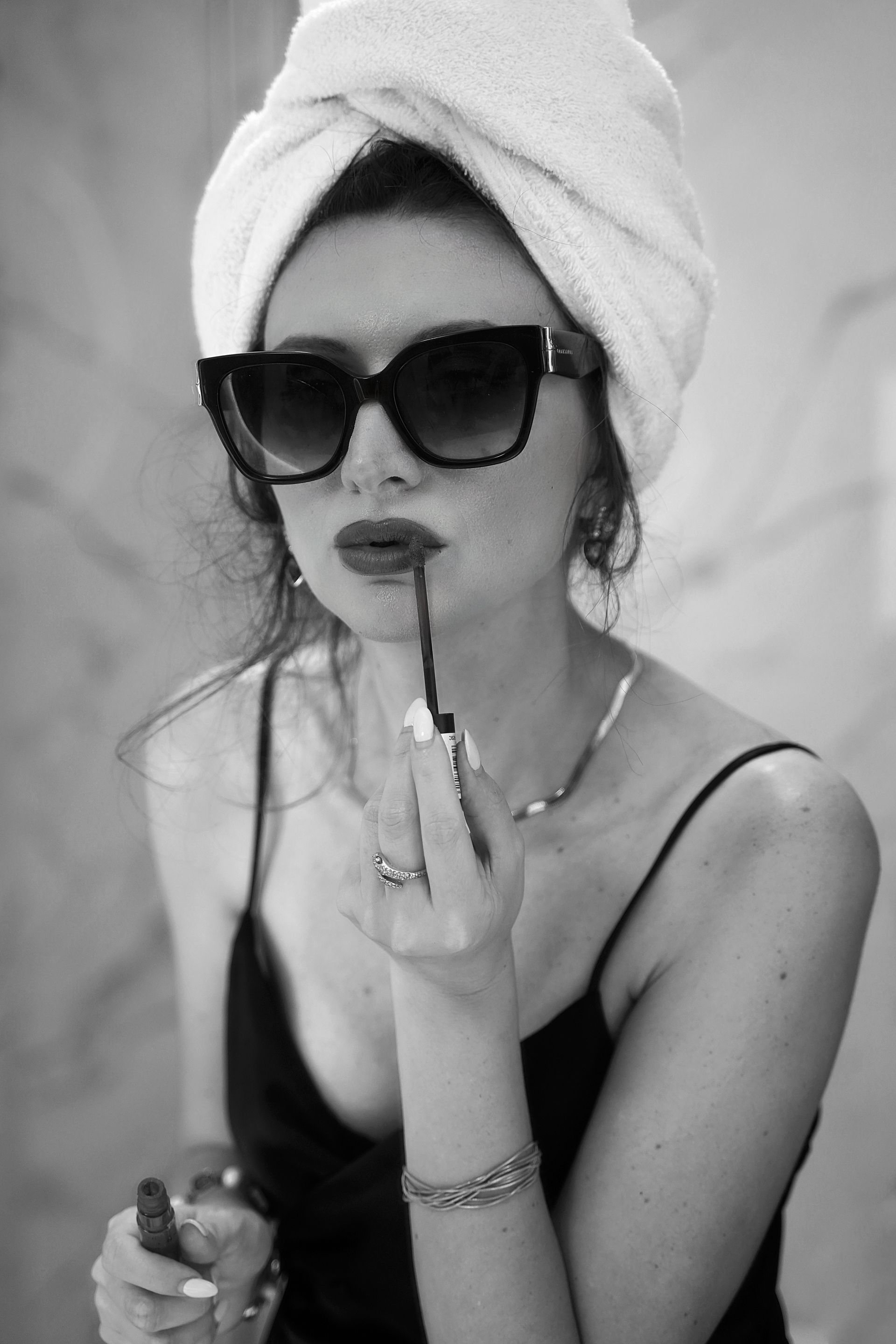 Donna con asciugamano, occhiali da sole e rossetto in bagno.