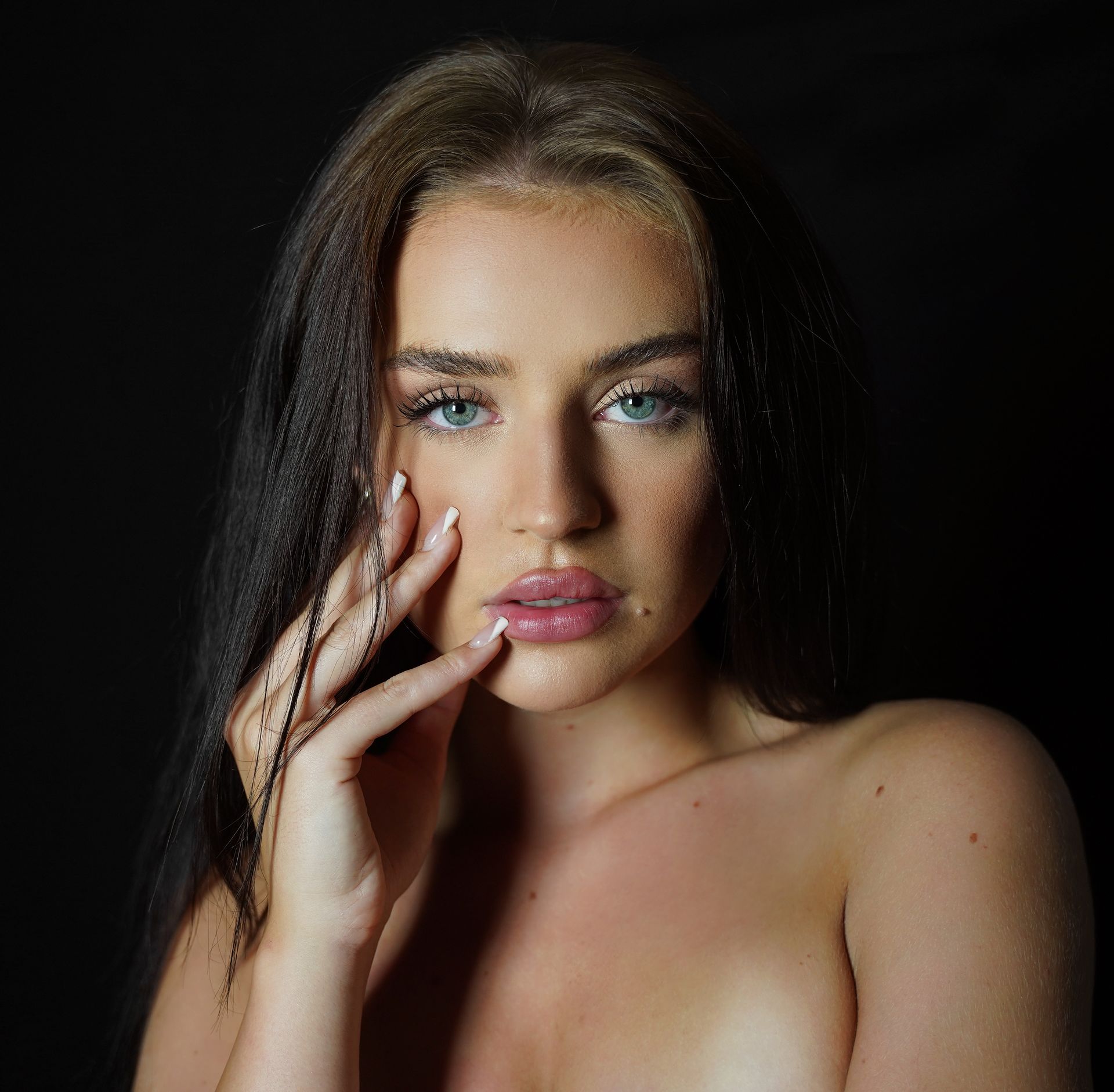 Donna con occhi azzurri, mano sul viso, capelli scuri, sfondo scuro.