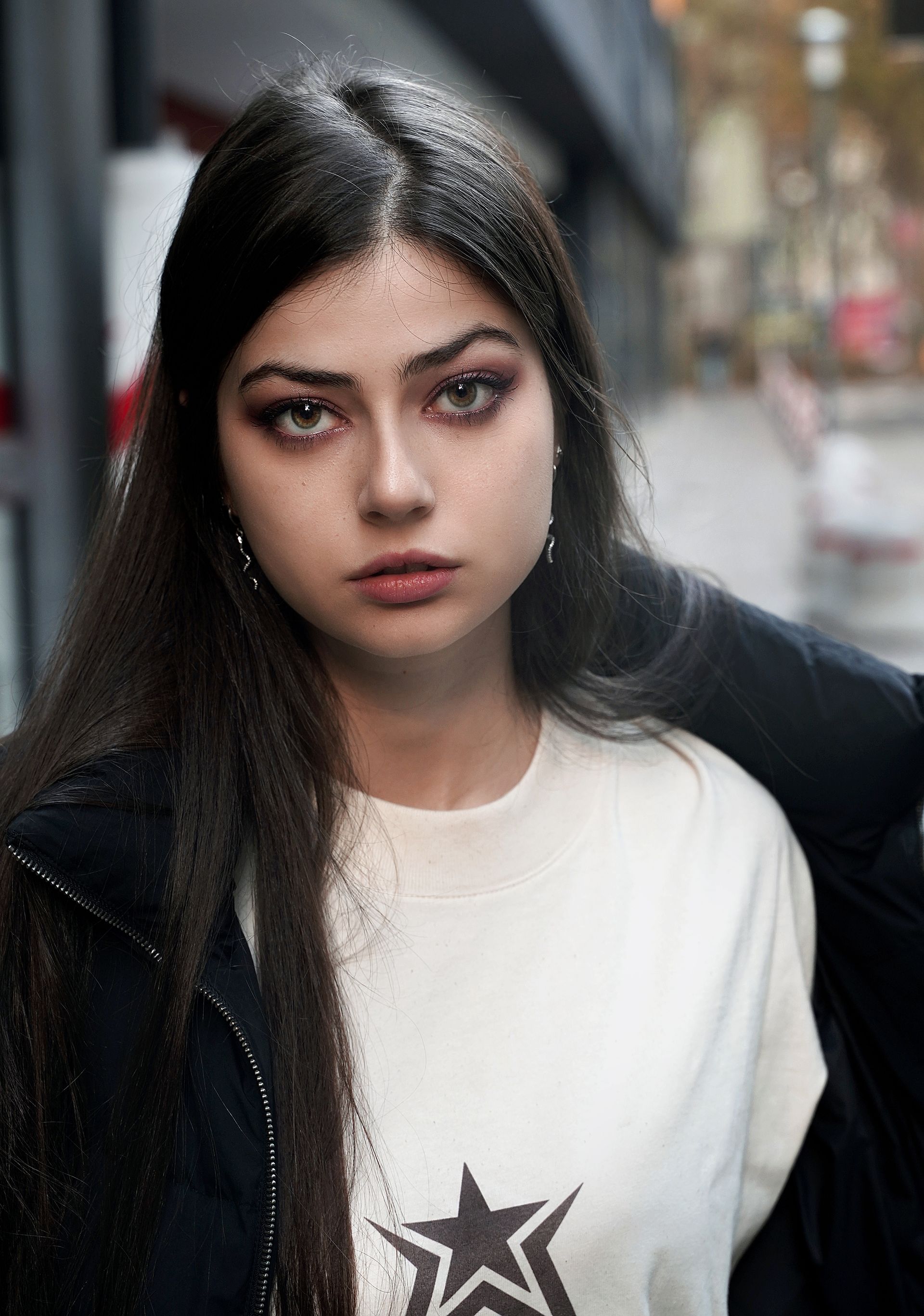 Giovane donna con capelli scuri e trucco sugli occhi, indossa una maglietta bianca e una giacca scura.