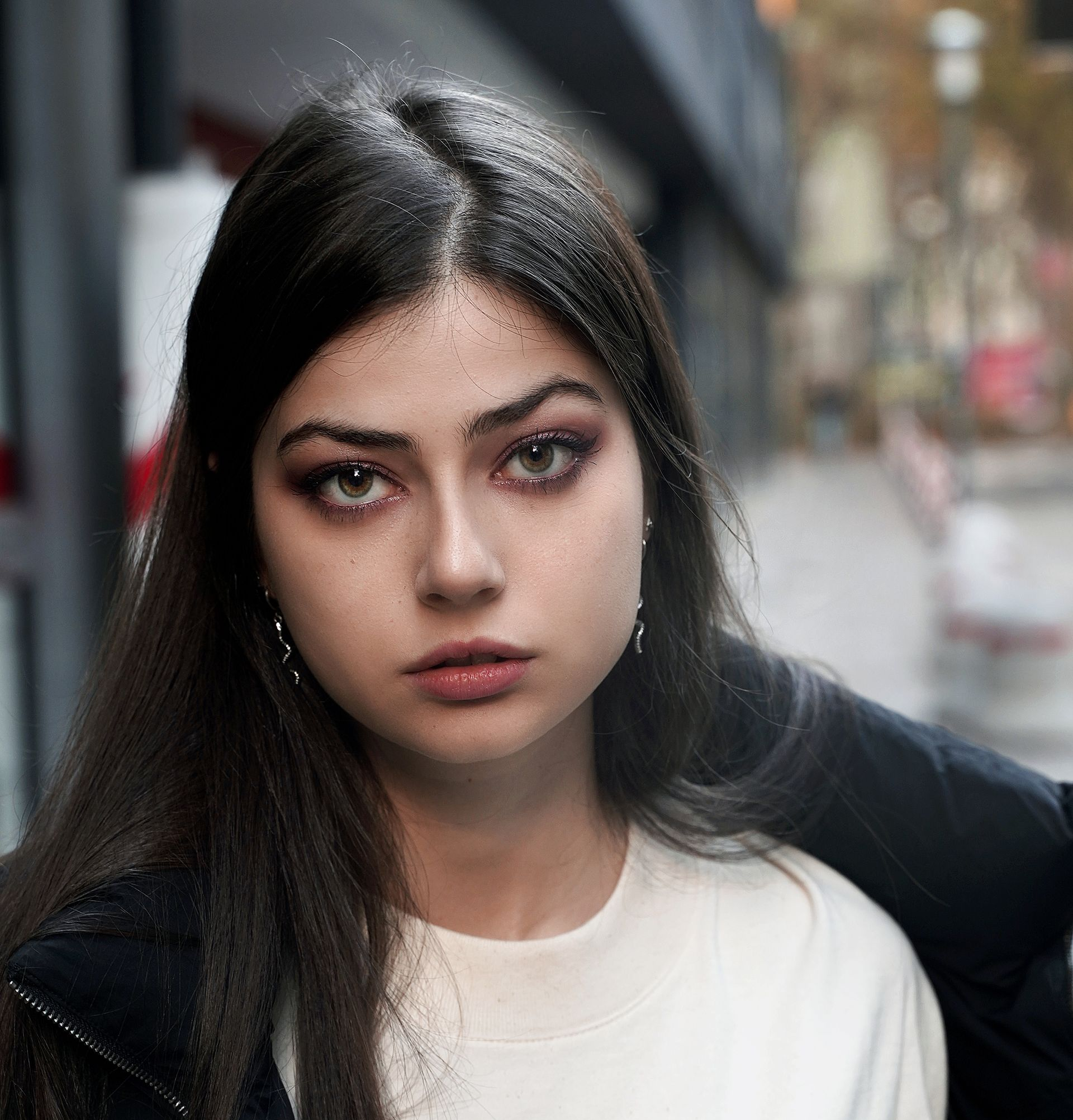 Donna con capelli scuri e trucco leggero davanti a un edificio, che guarda direttamente la telecamera.