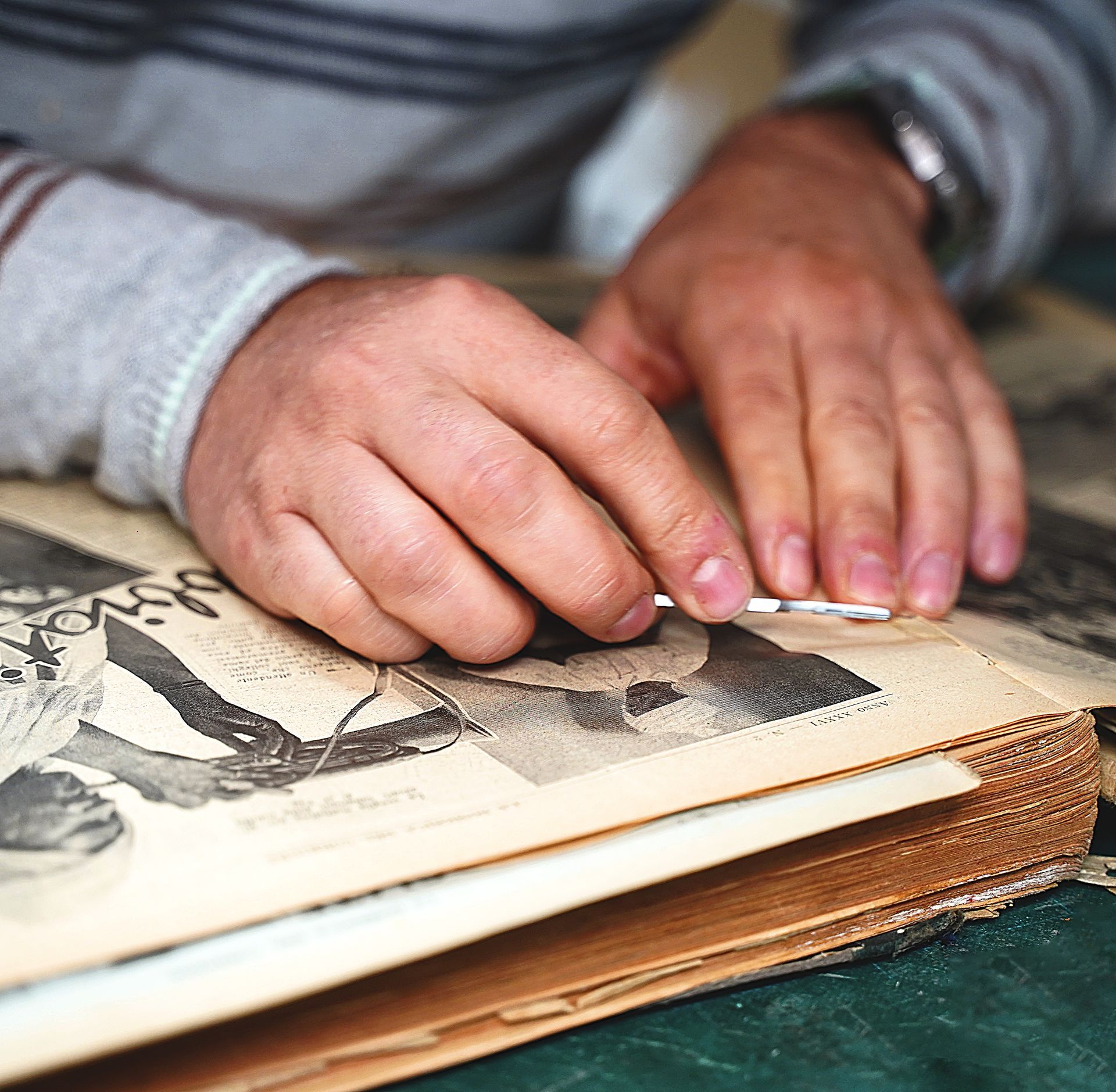 Mani di una persona con un orologio che restaira con cura un vecchio libro aperto.