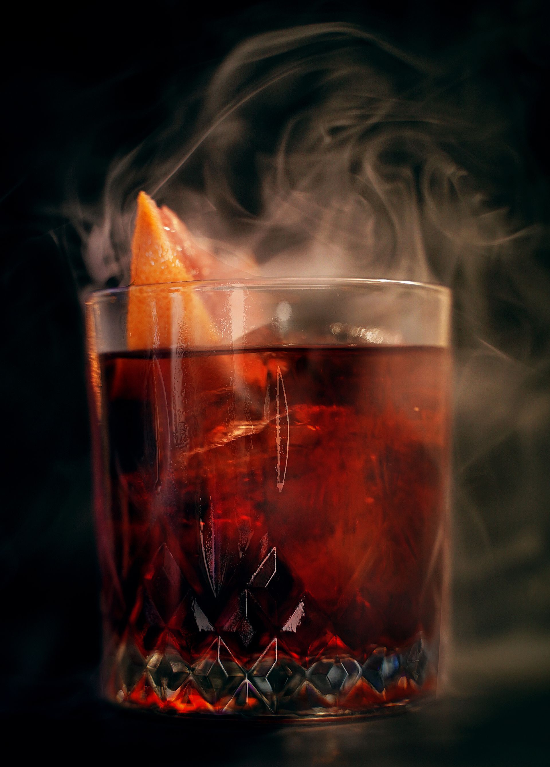 Cocktail affumicato in un bicchiere, guarnito con scorza d'arancia.