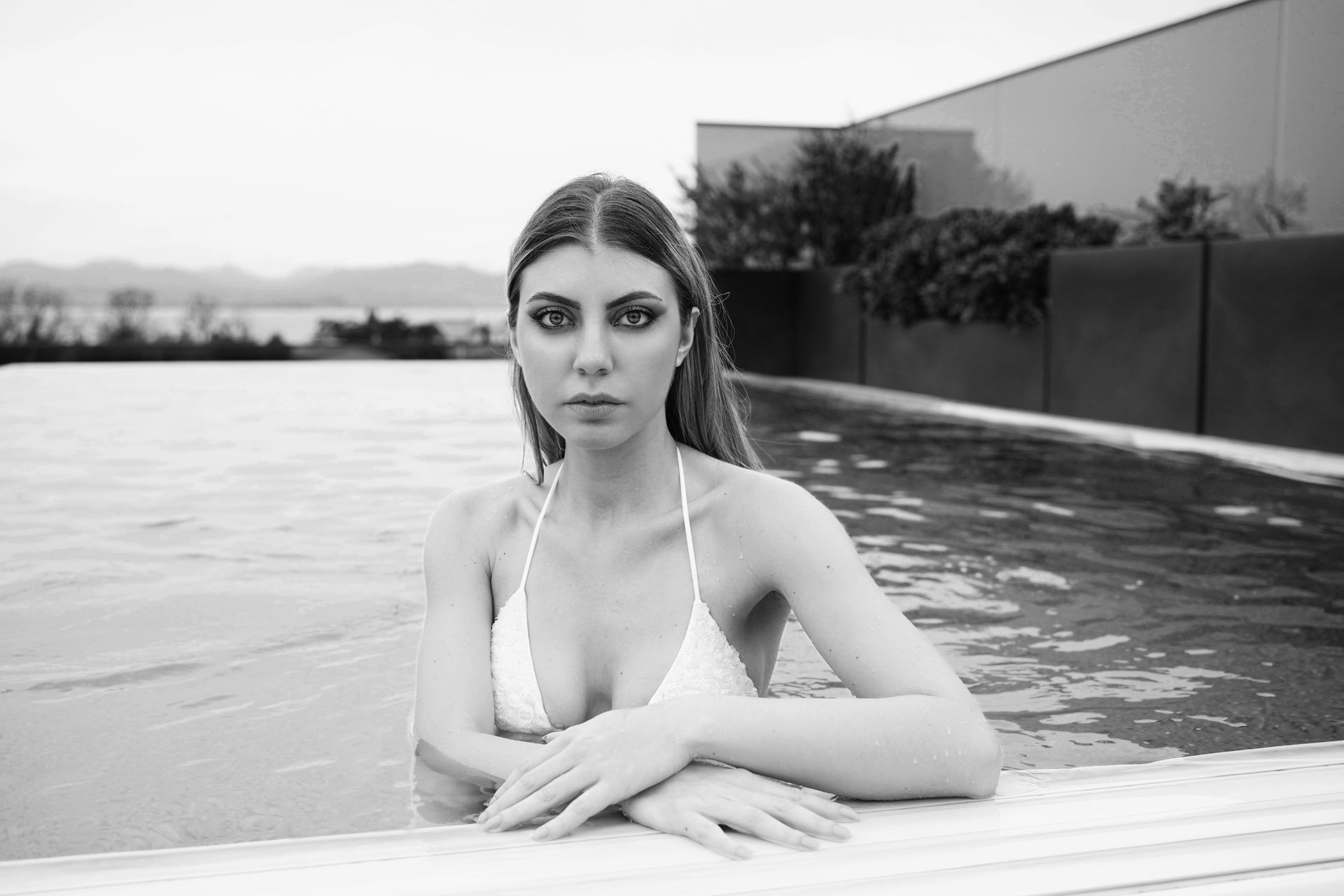 Donna in bikini bianco in piscina, che guarda la telecamera. Scala di grigi.