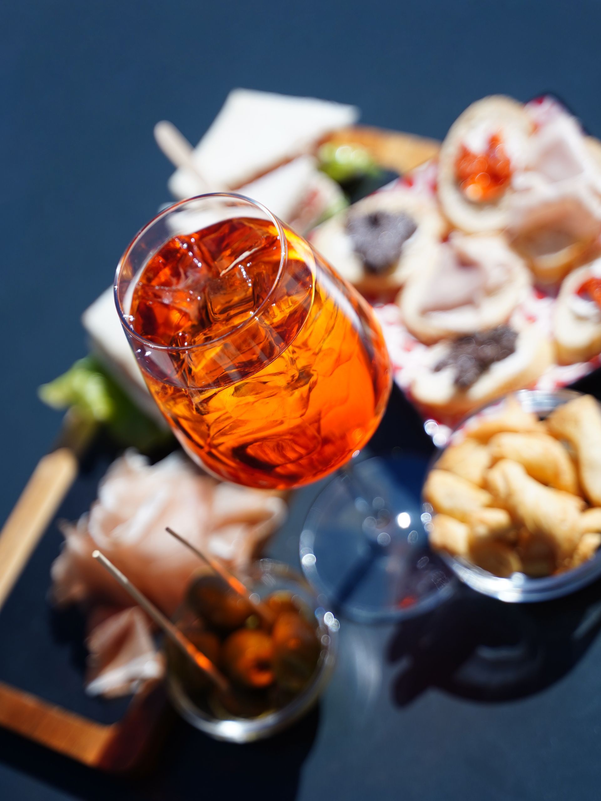 Spritz Aperol servito in un bicchiere con ghiaccio, accompagnato da stuzzichini come olive e stuzzichini.