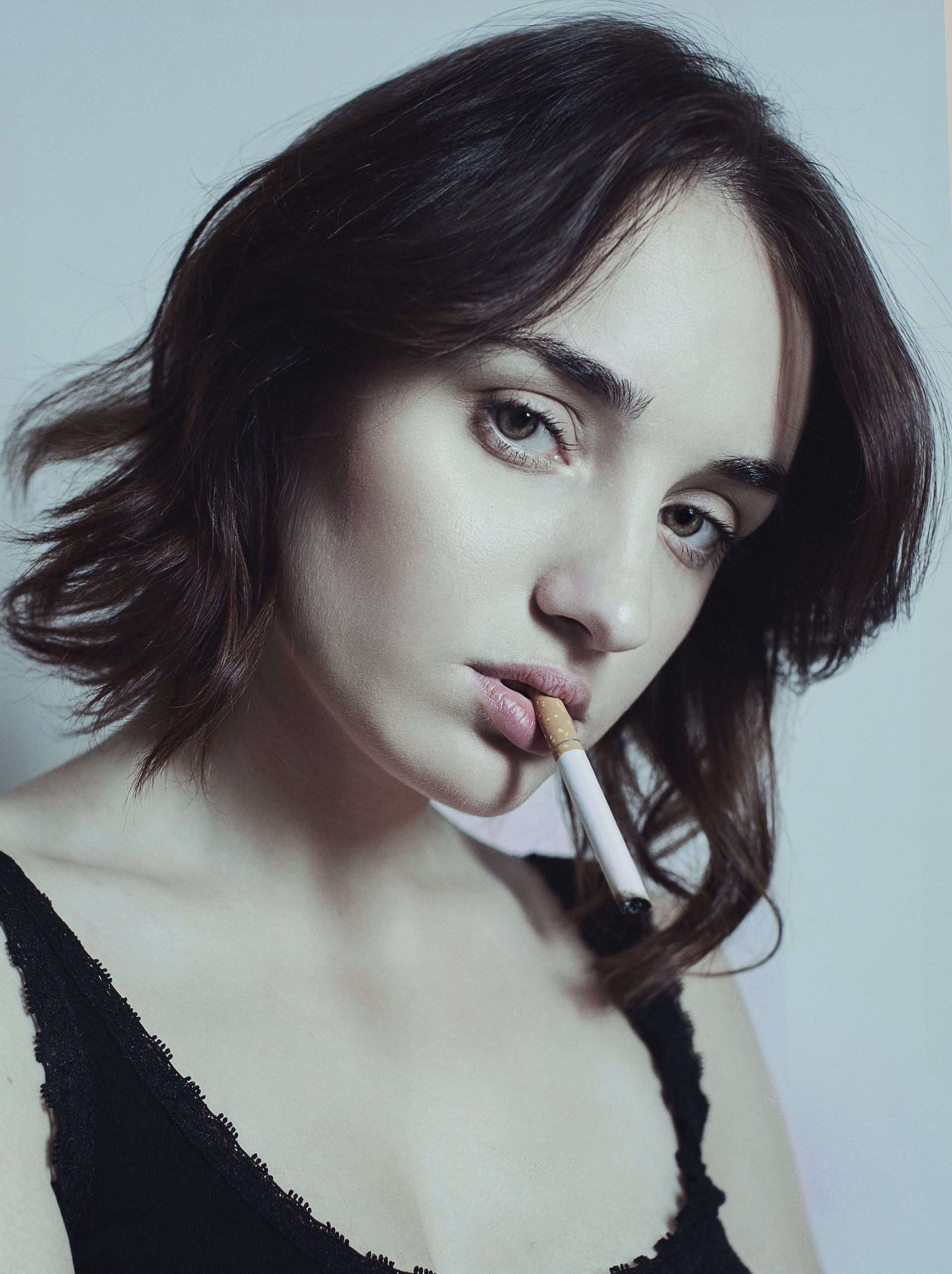 Donna con i capelli scuri, sigaretta in bocca, che guarda direttamente l'osservatore. Indossa una canotta nera.