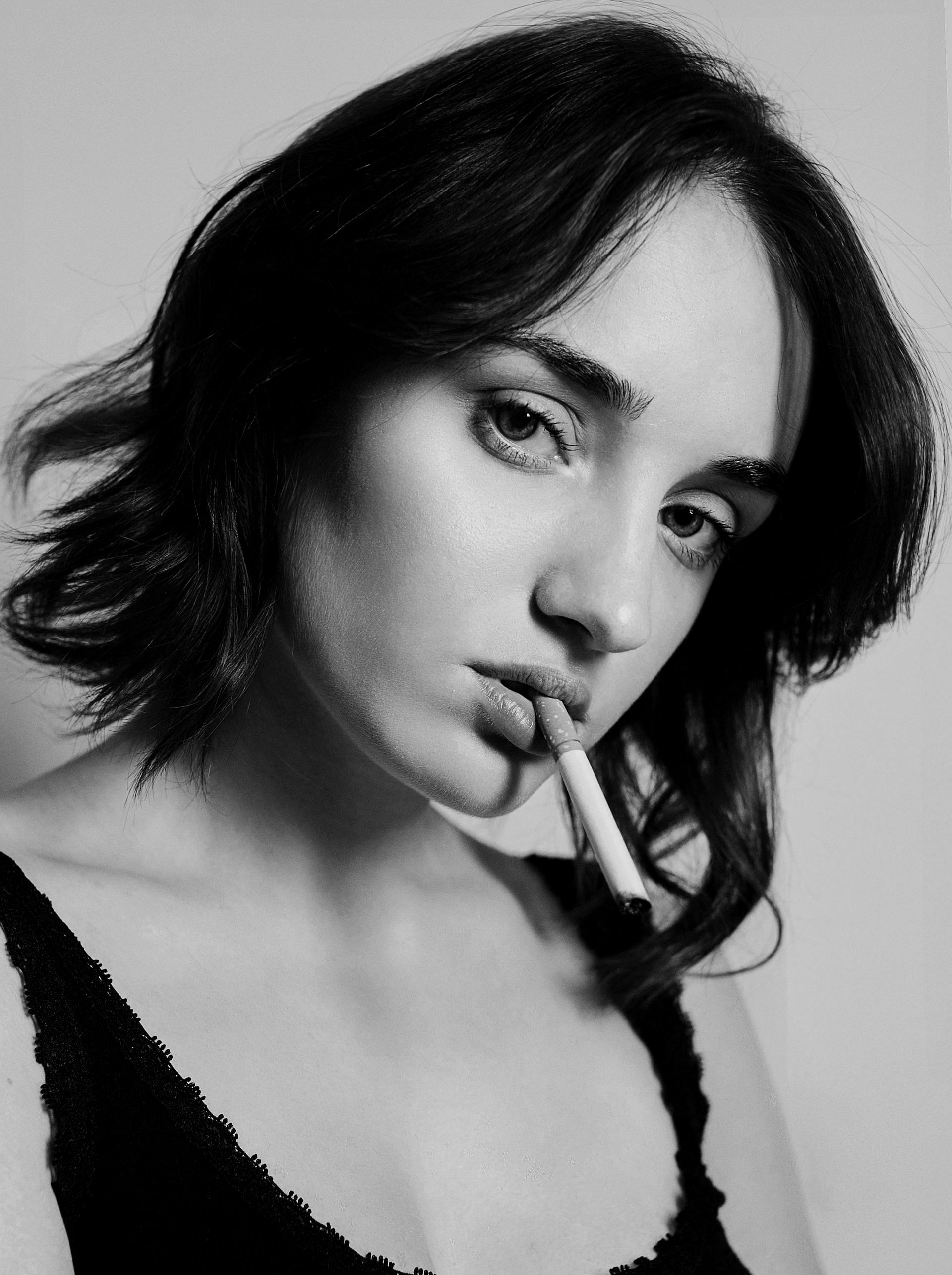 Donna con i capelli corti, sigaretta in bocca, che guarda la telecamera. Foto in bianco e nero.