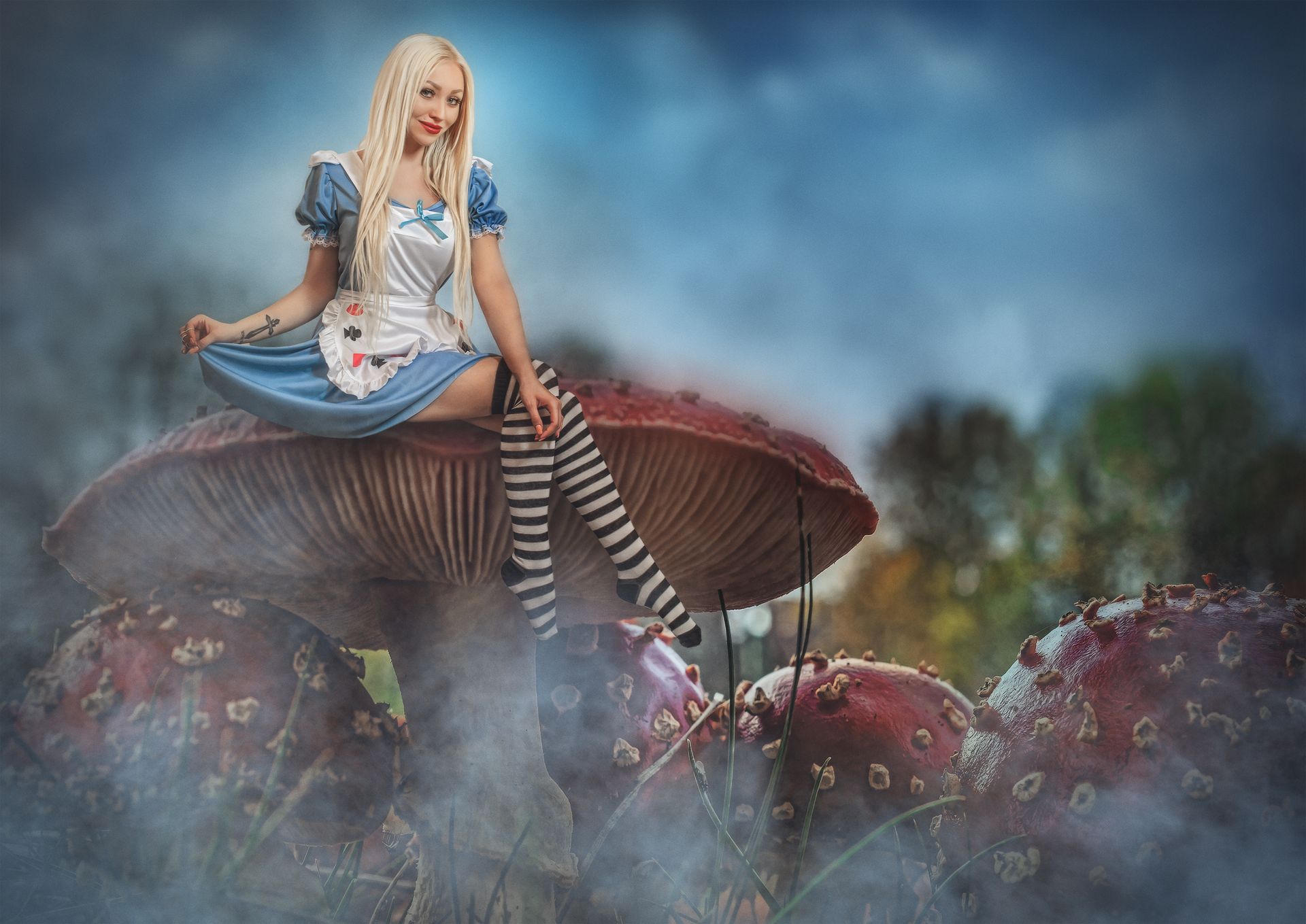 Donna in costume da Alice, seduta su un fungo gigante, circondata dalla nebbia.