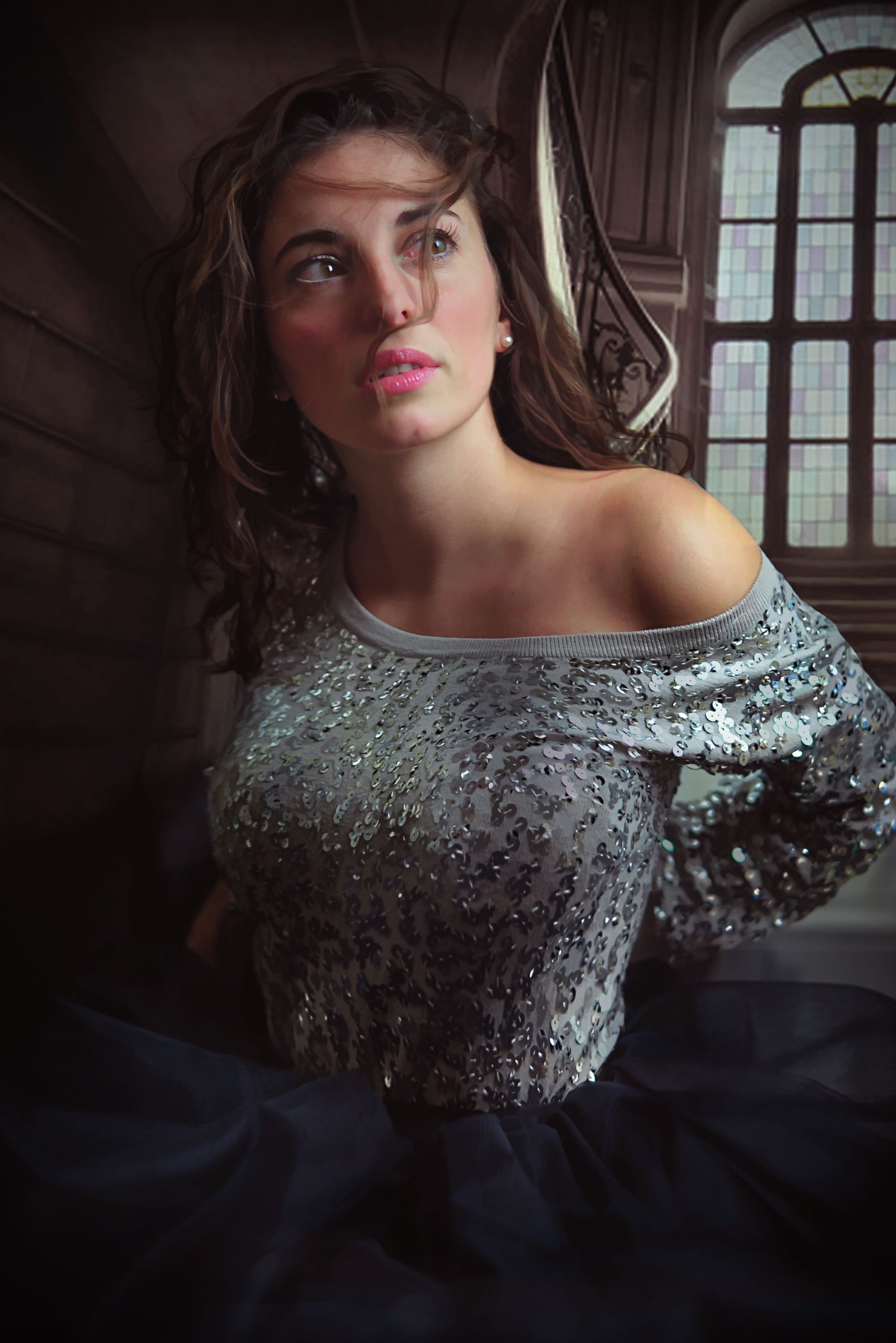 Donna con abito scintillante appoggiata alle scale, guarda verso l'alto.