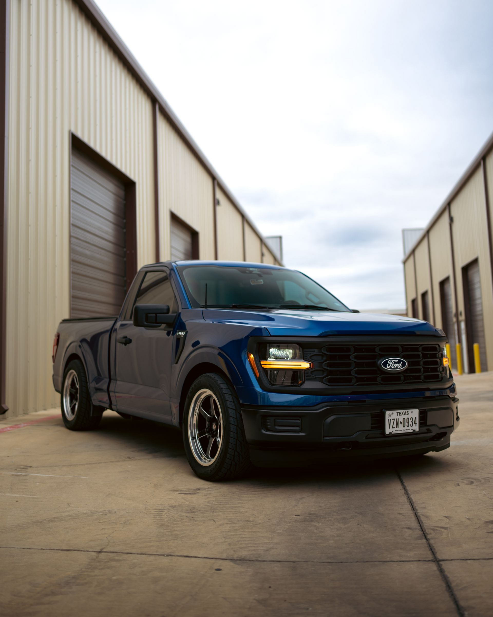 Blue pickup truck parked between warehouse buildings on a concrete lot