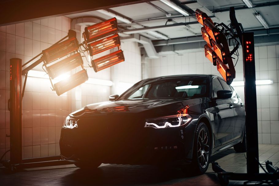 A car is sitting under a heat lamp in a garage.