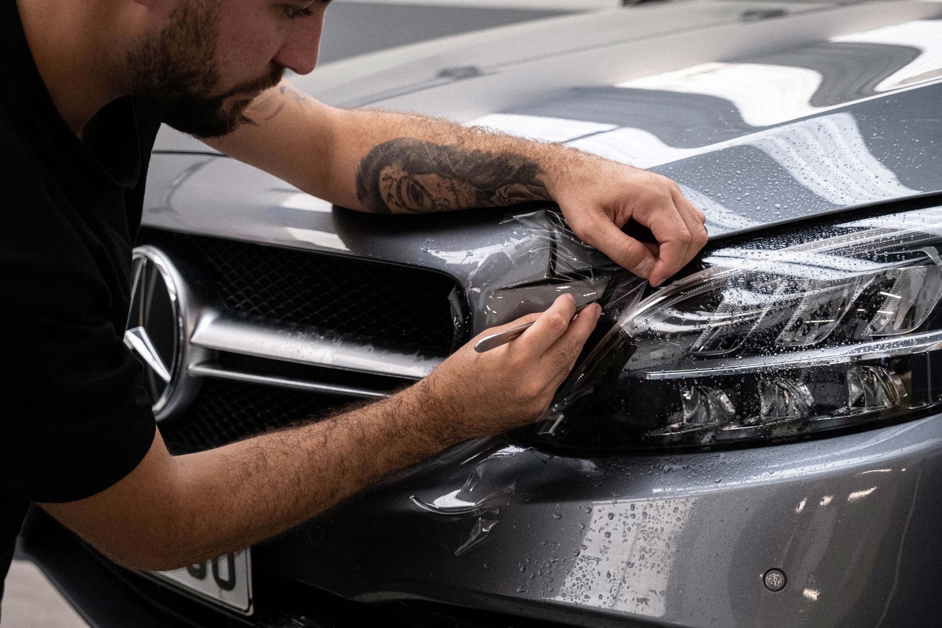 A man is applying a protective film to the headlights of a mercedes benz.