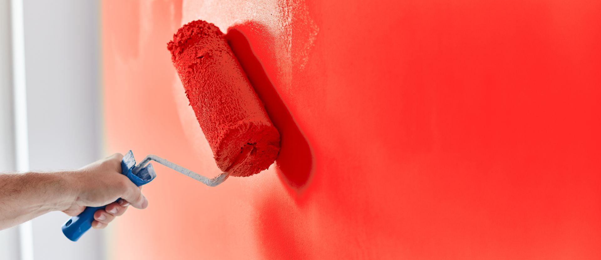A hand painting a wall red with a paint roller.