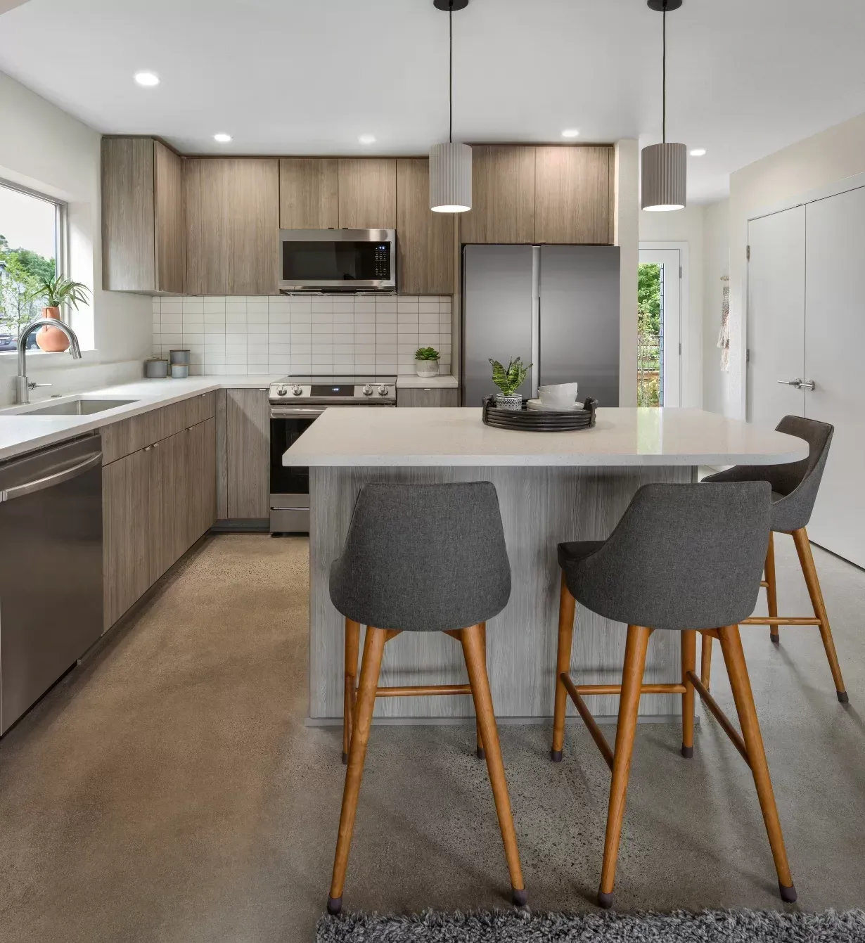 Modern kitchen with gray cabinets, island, stainless steel appliances, and three bar stools.